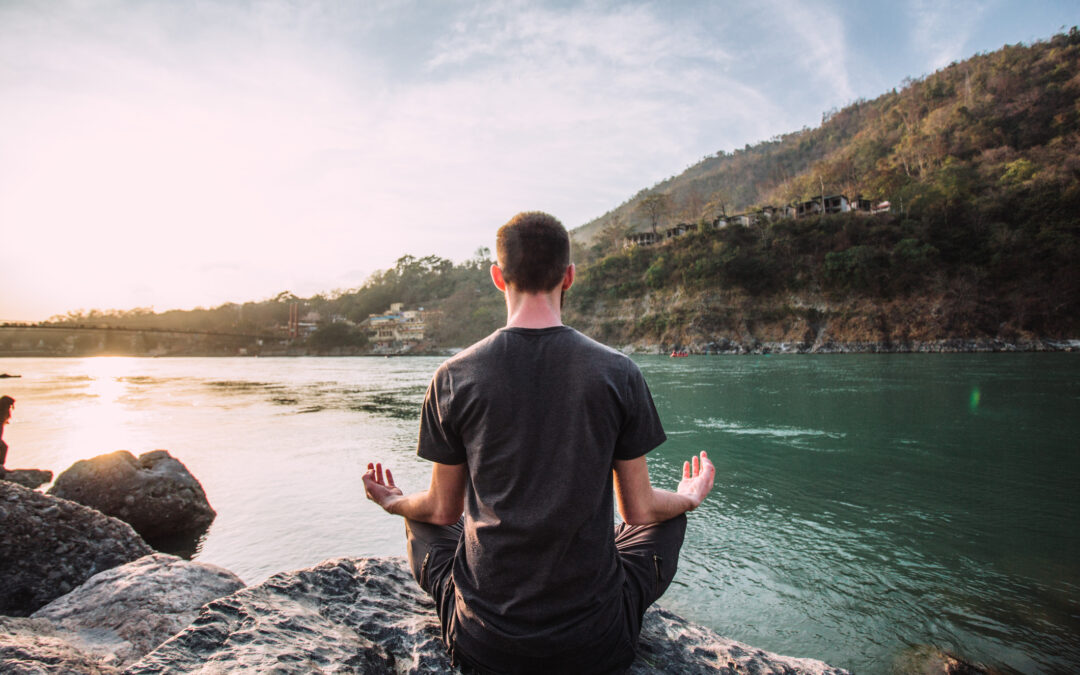 A young man meditates in a lotus position over the Ganges river in Rishikesh at the sunset.